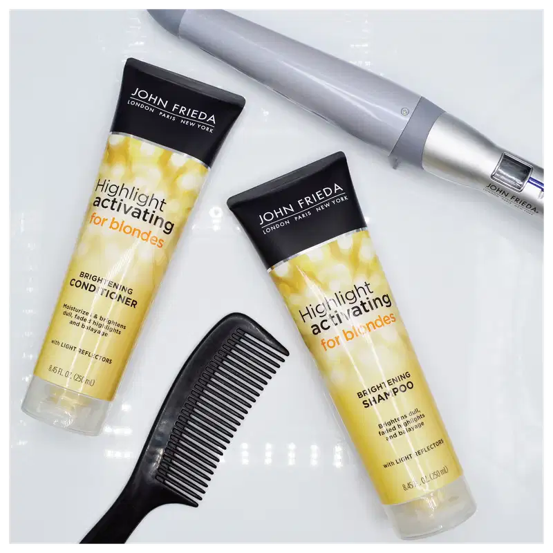 Imagem do shampoo e do condicionador da linah deitados em uma superfície plana da cor branca. Ao redor um pente preto e um modelador de cachos.