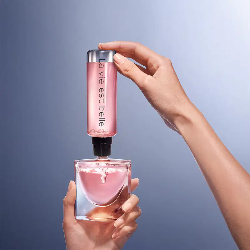 Frasco de perfume Lancôme com tampa prateada e corpo de vidro transparente contendo líquido rosa. Rótulo com nome da marca visível na parte inferior do frasco.