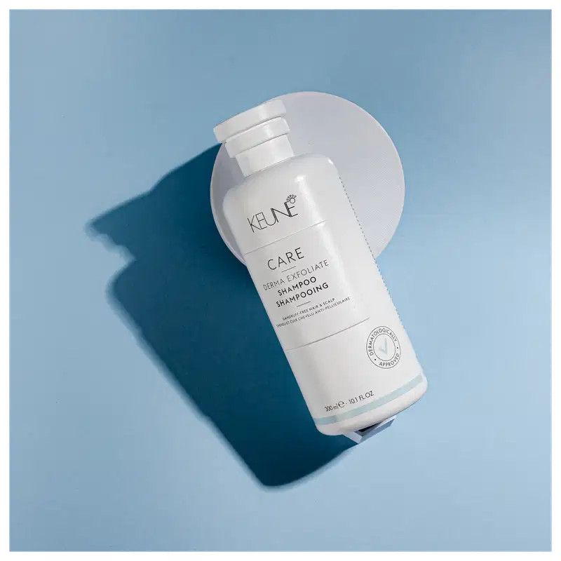 Frasco branco de shampoo Keune Care Derma Exfoliate, com rótulo em preto e branco indicando o nome do produto e sua função de remover caspa do couro cabeludo.