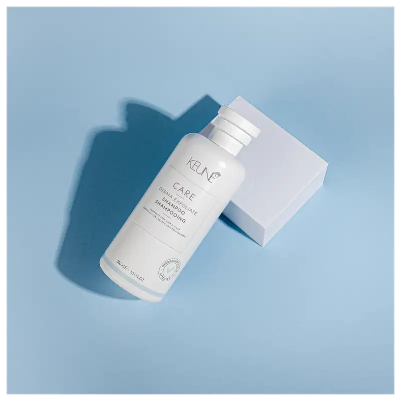 Frasco branco de shampoo Keune Care Derma Exfoliate, com rótulo em preto e branco indicando o nome do produto e sua função de remover caspa do couro cabeludo.