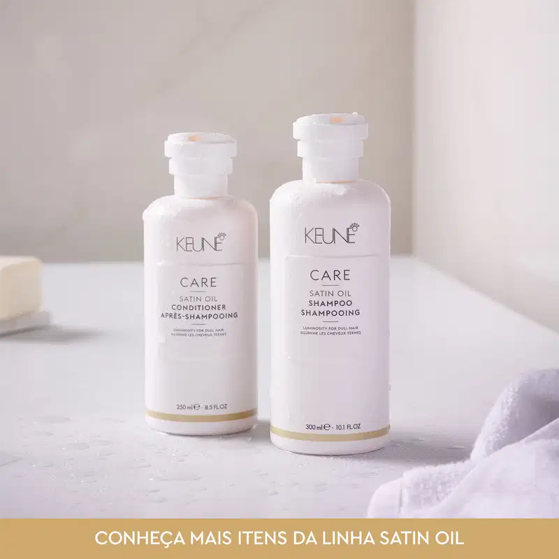 Dois frascos brancos da linha Satin Oil da Keune, contendo condicionador e shampoo. Os frascos possuem rótulos com o nome da marca e do produto, em cores branca e dourada.