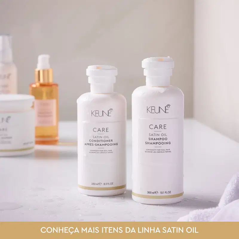 Dois frascos brancos da linha Satin Oil da Keune, um contendo condicionador e outro shampoo, com rótulos em branco e dourado destacando a marca e o nome da linha.