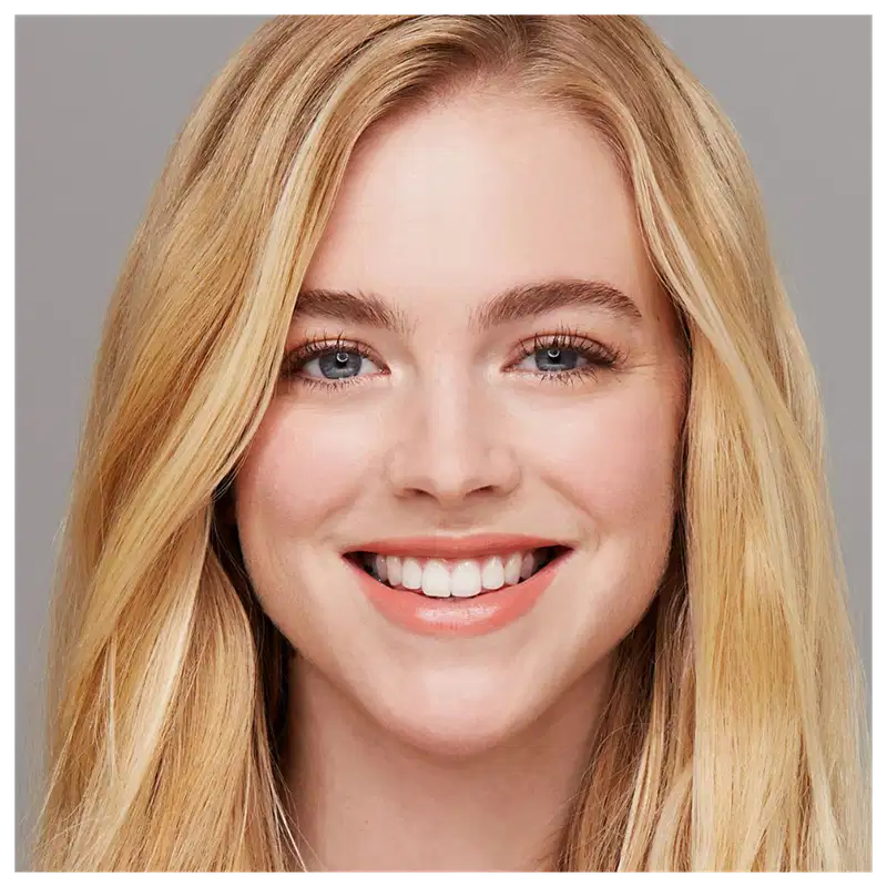 Close-up do rosto sorridente de uma mulher loira jovem com olhos azuis e dentes brancos. Ela tem uma expressão alegre e um visual natural e atraente.