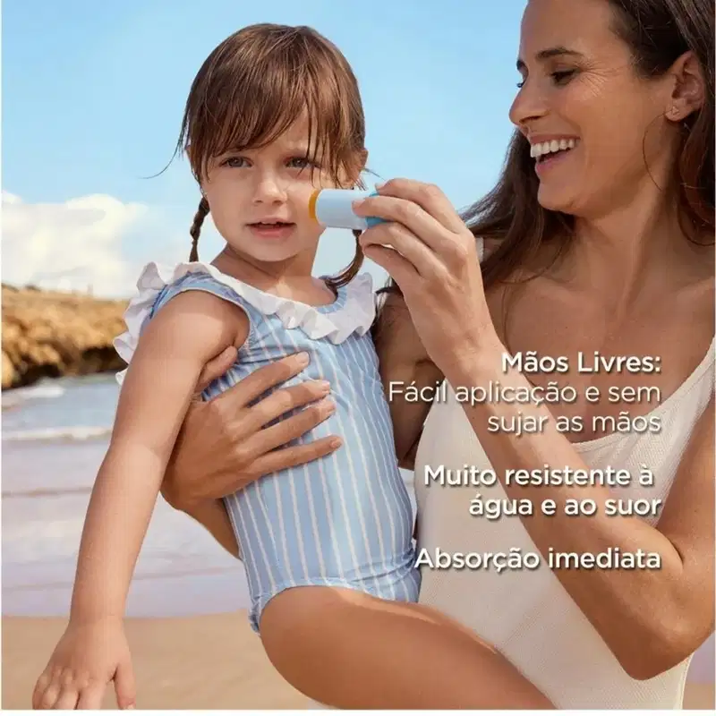 Mãe aplicando protetor solar em stick no rosto de criança na praia, com mar e areia ao fundo sob céu azul.