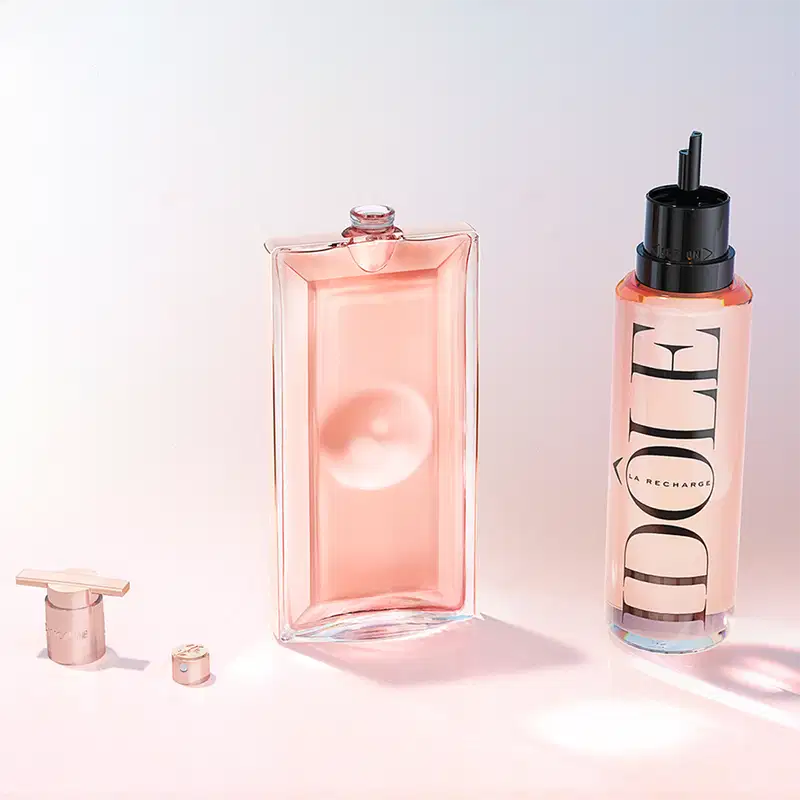 Frascos de perfume e embalagem de produto Lancôme com design moderno e cores suaves de rosa e branco. Destaque para o frasco de perfume com formato geométrico e a embalagem com o logotipo da marca.