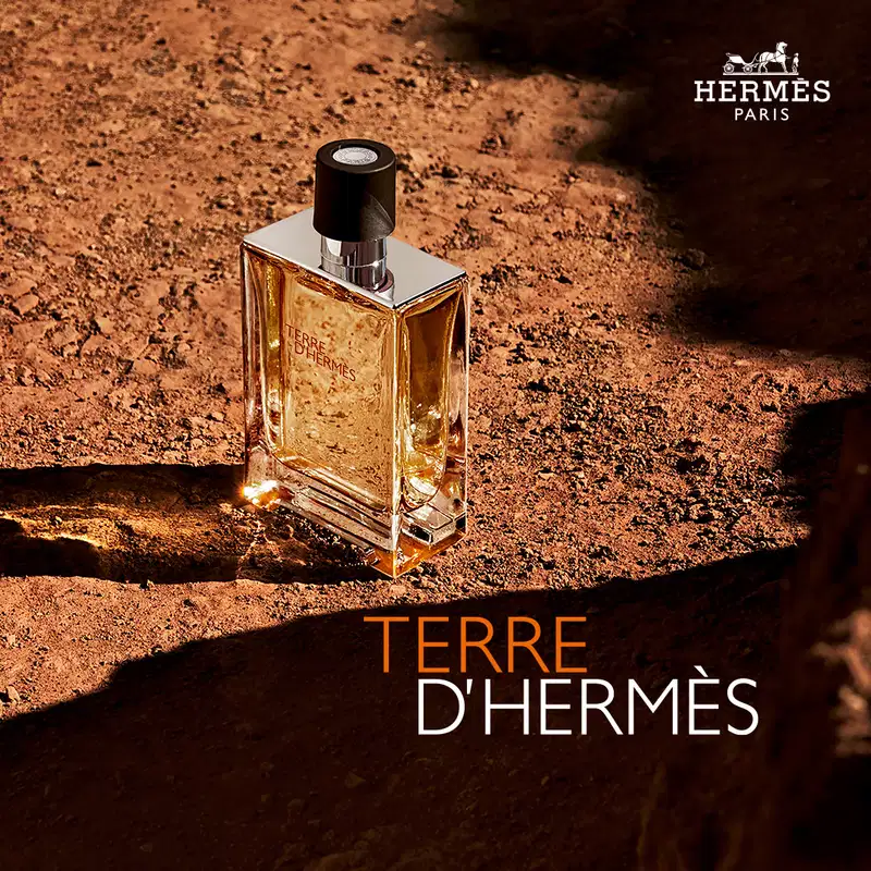 Frasco de perfume Terre d'Hermès com design elegante e minimalista em vidro transparente. Rótulo com texto em vermelho destaca o nome da fragrância.