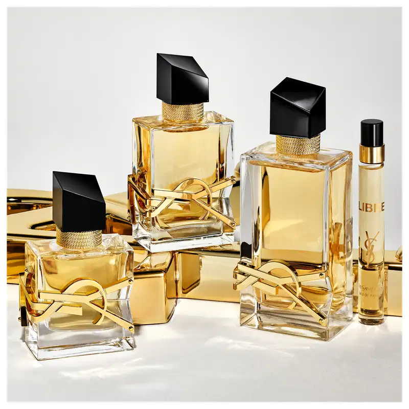 Fragrâncias Yves Saint Laurent em embalagens de vidro e metal dourado, com detalhes pretos e rótulos destacados. Diversos frascos de diferentes tamanhos e formatos, exibindo a marca e o nome dos produtos.