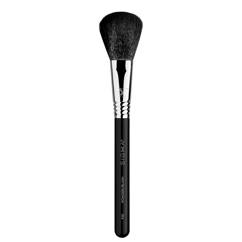 A imagem mostra um pincel de maquiagem de alta qualidade da marca Sigma Beauty. O pincel tem um cabo preto com o nome "Sigma" e a descrição "Powder Brush F10" gravados nele. A parte superior possui cerdas densas e macias em formato arredondado.