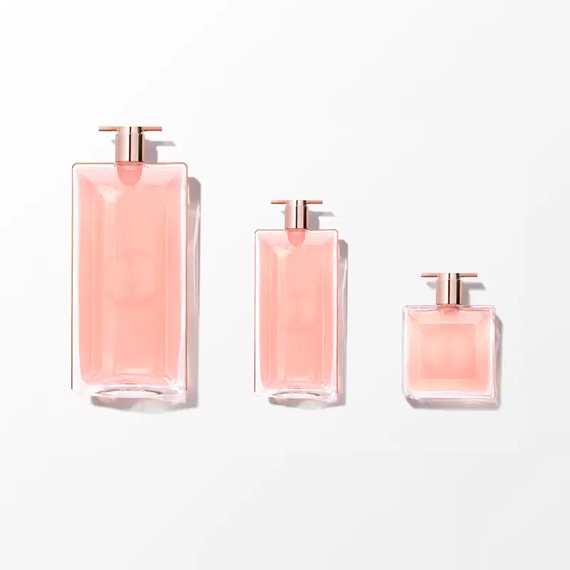 Três frascos de perfume Lancôme em diferentes tamanhos, com embalagens de vidro rosa translúcido e detalhes em metal rosé. Os frascos possuem formato geométrico e elegante, com bombas doseadoras.