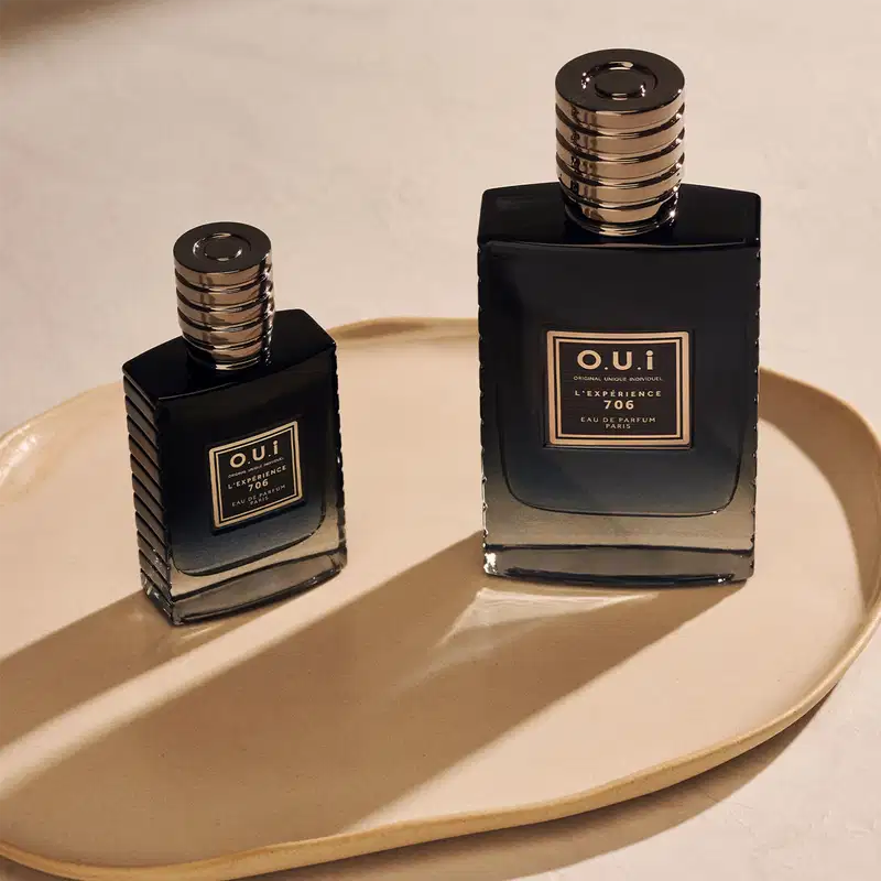 Dois frascos de item de perfumaria da marca O.U.I. em uma bandeja dourada. Os frascos possuem design elegante com detalhes em preto e dourado, indicando tratar-se de uma fragrância sofisticada. O ambiente sugere um cenário de luxo e exclusividade.