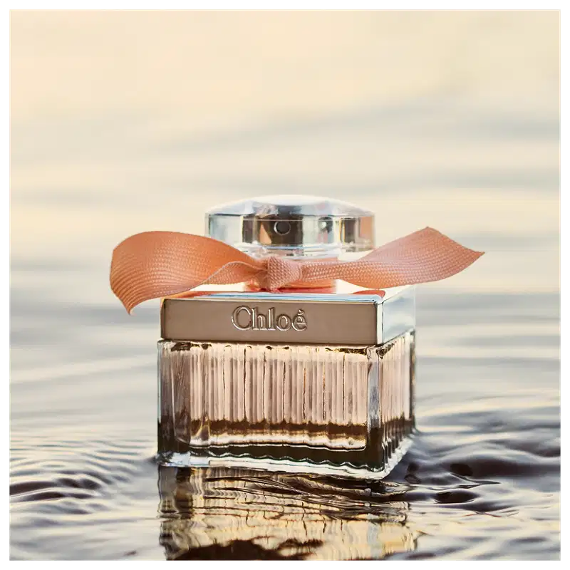 Frasco de perfume Chloé com tampa prateada e laço laranja, em embalagem de vidro com listras verticais, exibindo o nome da marca em destaque.