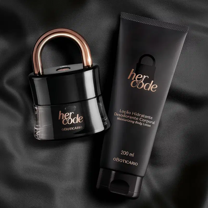 Dois itens da marca Her Code em embalagens pretas com letras douradas, sendo um vidro em formato de cadeado com arco dourado  contendo Eau de Parfum e uma bisnaga contendo loção hidratante corporal. O fundo da imagem é um tecido preto.