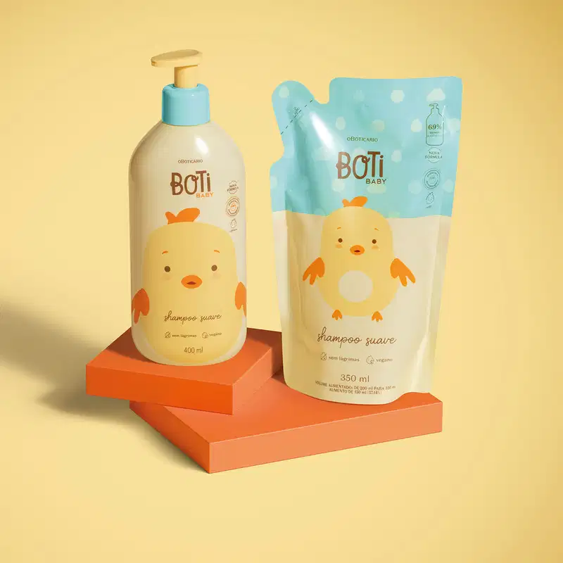 Dois itens Boti Baby em embalagens em tons de amarelo, azul e laranja com ilustração de passarinho amarelo, sendo um frasco com bomba dosadora de shampoo e um refil em sachê sobre plataforma e fundo em tons de laranja.