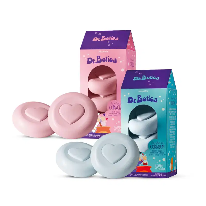 Caixa rosa e azul escuro ao lado de dois sabonetes em barra na cor rosa com coração gravado e caixa azul claro e azul escuro ao lado de dois sabonetes em barra na cor azul com coração gravado, ambos da marca Dr. Botica.