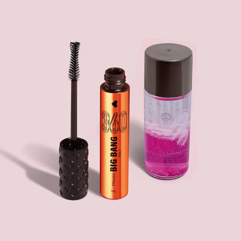 Máscara de cílios Big Bang 360 em embalagem laranja com tampa com textura de corações e aplicador pretos acompanhado de um frasco com líquido roxo e incolor e tampa preta de demaquilante bifásico, ambos da marca Quem Disse, Berenice? em fundo cinza claro.