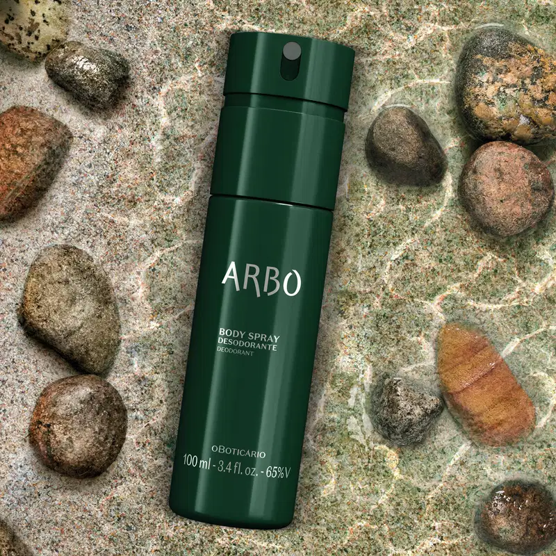 Embalagem verde escura de item de body splash Arbo Forest sobre espelho d'água com pedras no fundo em tons de cinza, em ambiente natural.