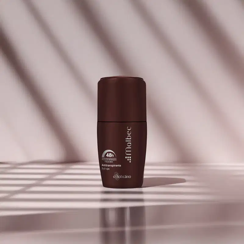 Imagem de embalagem de desodorante antitranspirante roll-on na cor vinho da marca Malbec sobre superfície clara com sombras suaves, em ambiente iluminado e minimalista.
