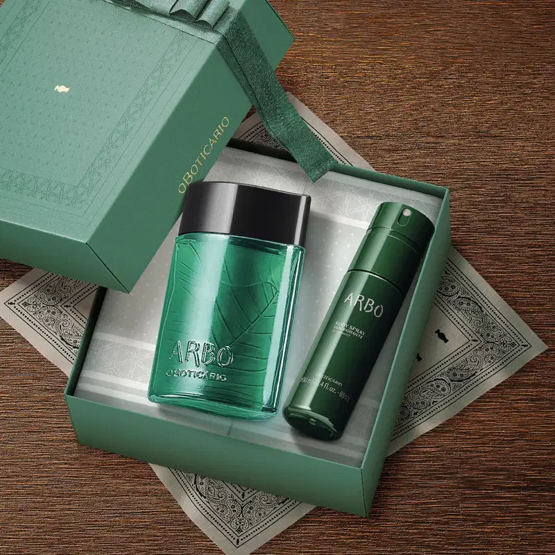 Imagem de caixa verde contendo um frasco de desodorante colônia Arbo e body spray da mesma marca, sobre superfície de madeira com detalhes decorativos.