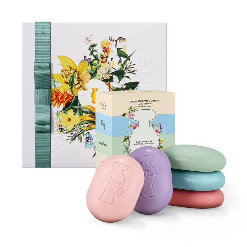 Caixa de presente com sabonetes perfumados em formatos de ovos coloridos, embalados em caixa com ilustração floral. Conjunto de sabonetes em tons pastel de rosa, roxo, azul e vermelho.