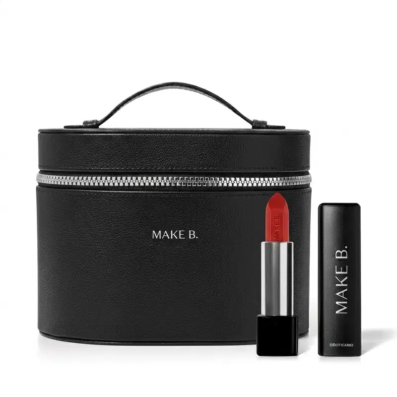 Frasqueira de maquiagem preta com zíper e alça, com aspecto rígido e estruturado feita em tecido tipo couro e logo Make B. em hot stamping prata e um batom vermelho vivo aberto com a bala visível, corpo prateado e base preta com tampa preta ao lado.
