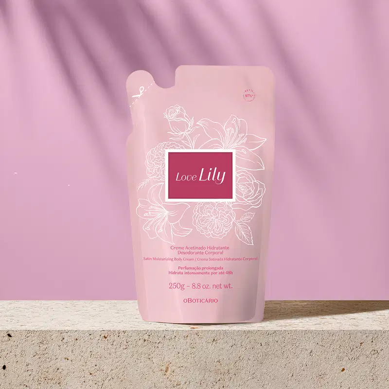 Refil de creme acetinado desodorante hidratante corporal da marca Love Lily em sachê na cor bege com detalhes dourados e rótulo marrom claro. O produto está em superfície de mármore e fundo rosado com sombras de folhagens.