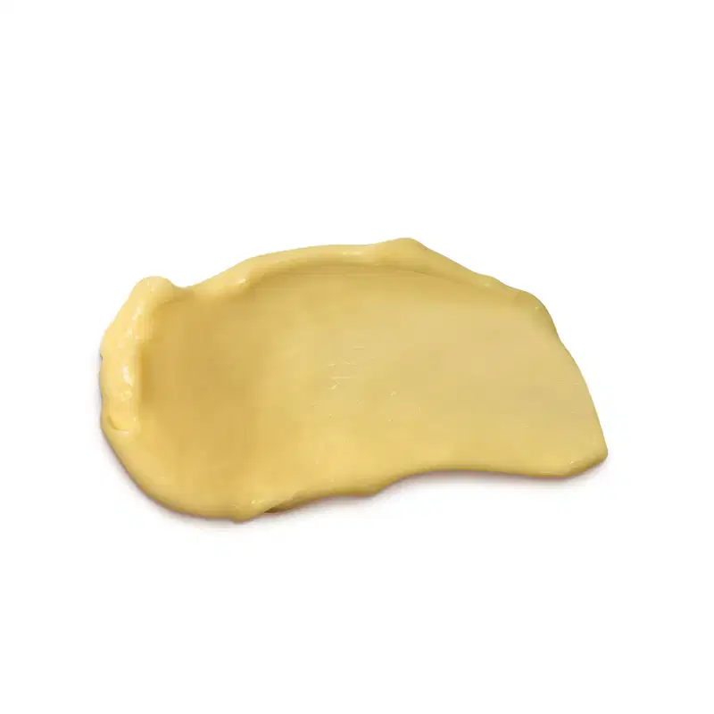 Textura cremosa e amarelada de condicionador da marca Cuide-se Bem Feira Banana, com aparência densa e uniforme, espalhada em superfície branca e lisa.