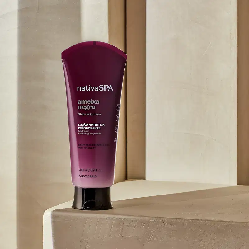 Bisnaga com degradê de roxo escuro e branco, tampa preta e letras douradas, brancas e pretas de loção nutritiva corporal da marca Nativa SPA Ameixa Negra. posicionado em superfície bege clara, com paredes e portas de madeira ao fundo em tons neutros.