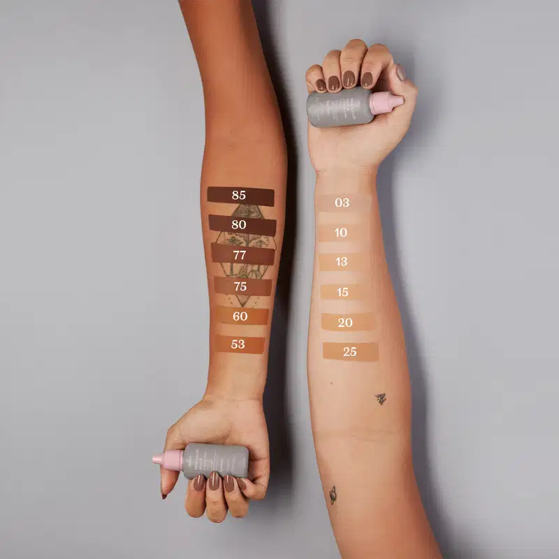 Dois braços femininos estão estendidos lado a lado e, em cada um deles, amostras das cores da base líquida e corretivo Reboco HD na cor 80 da marca Intense, mostrando como elas ficam em cada tom de pele.