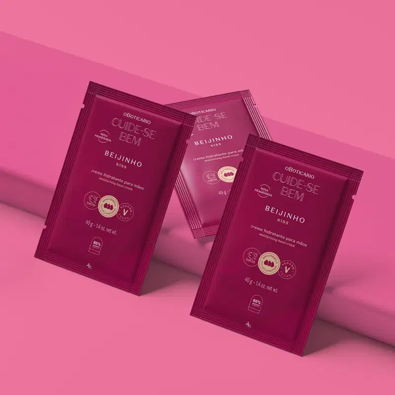 Três refis de creme hidratante para as mãos da marca Cuide-se Bem Beijinho em sachês de 40g na cor vinho com letras bege. Eles estão em fundo rosa.