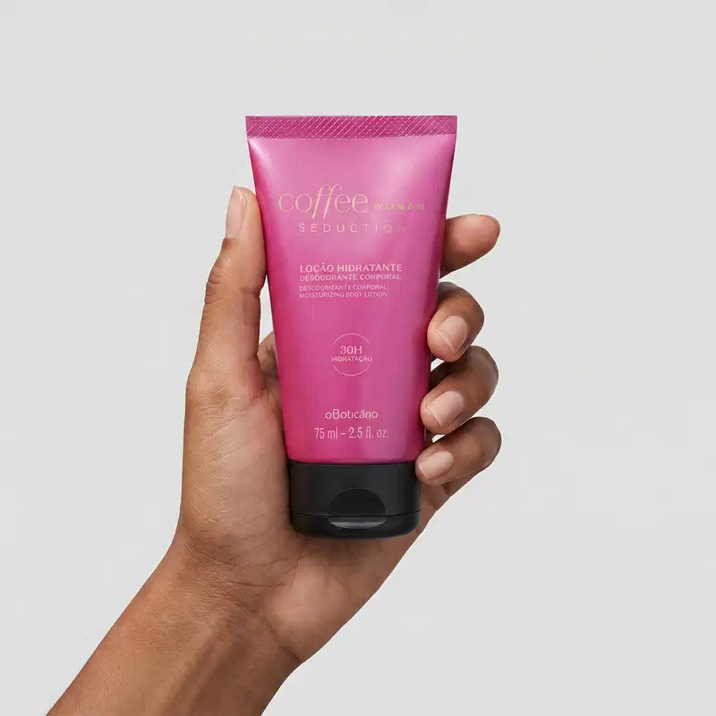 Recipiente de plástico rosa com rótulo "Coffee Woman Seduction" contendo loção hidratante desodorante corporal. O produto é segurado por uma mão feminina de pele negra em primeiro plano contra um fundo branco liso.
