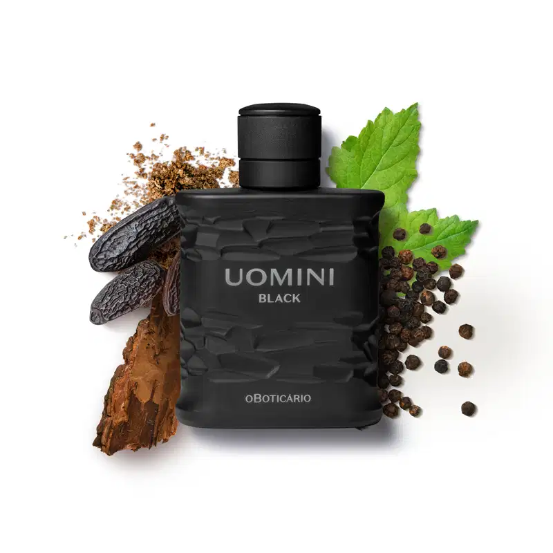 Frasco retangular preto com texturas onduladas, tampa preta e letras cinzas, contendo desodorante colônia da marca Uomini Black, rodeado por folhas verdes, grãos de pimenta, pedaços de madeira e fava de tonka.
