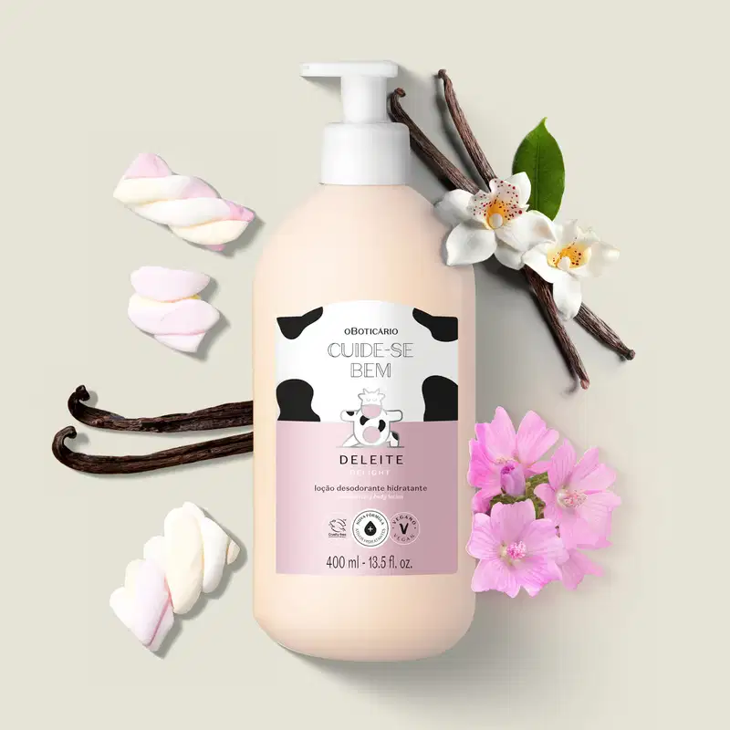 Frasco branco com bomba dosadora, rótulo branco e rosa com manchas pretas e com vaquinha ilustrada, de loção hidratante corporal Cuide-se Bem Deleite em ambiente com flores brancas, galhos de baunilha e marshmallows rosa, sobre superfície clara.