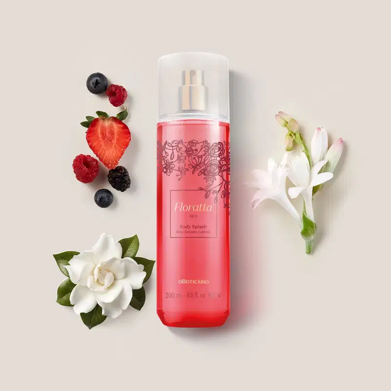 Frasco rosa com detalhes em vinho e letras douradas, pulverizador prateado e tampa cristal de body splash Floratta Red. cercado por frutas vermelhas, flores brancas e folhagens sobre fundo bege claro.