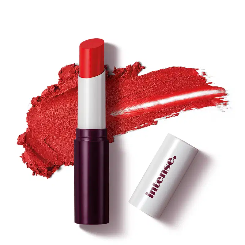 Batom Stick Glossy de cor vermelha da marca Intense em embalagem preta e branca com tampa branca e letras pretas. Ao fundo, há um rastro do produto, evidenciando a textura cremosa de cor vermelha e alta pigmentação.