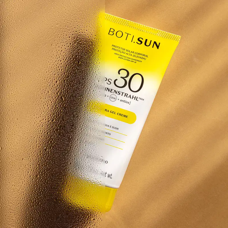 Bisnaga amarela e branca com tampa amarela e letras pretas contendo 200g de protetor solar corporal FPS 30 da marca Boti.Sun em um fundo bege com sombras onduladas.