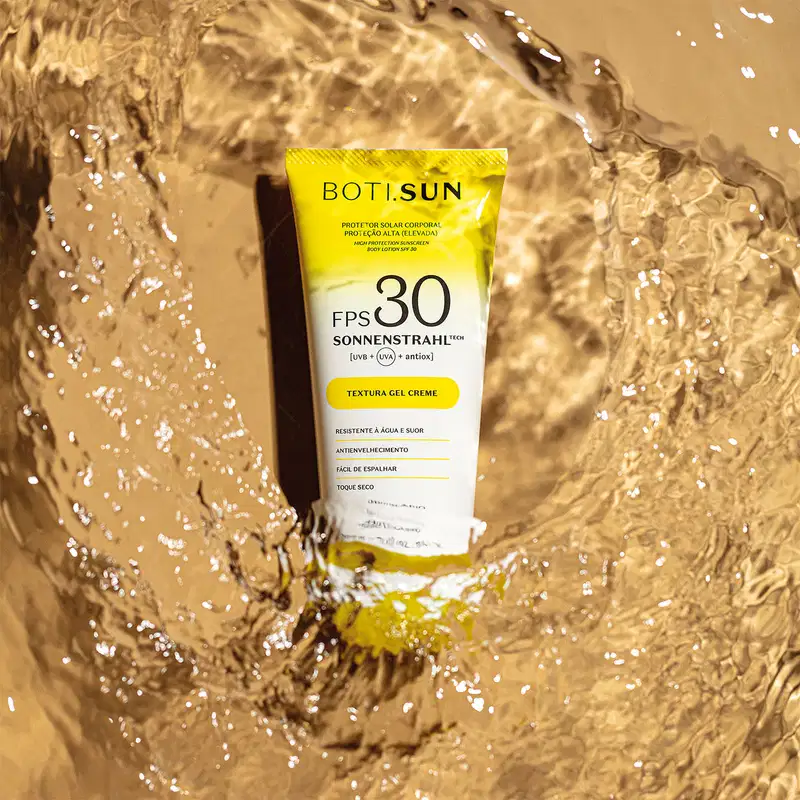 Bisnaga amarela e branca com tampa amarela e letras pretas de protetor solar corporal FPS 30 da marca Boti.Sun em um cenário d areia de praia molhada.