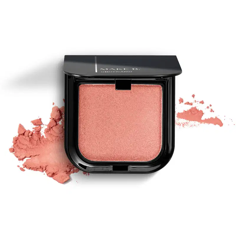 Blush em pó mate Luminoso Rose Make B. na cor rosa em estojo quadrado preto de cantos arredondados com espelho na tampa. Um pouco do produto está esfarelado ao lado da embalagem.