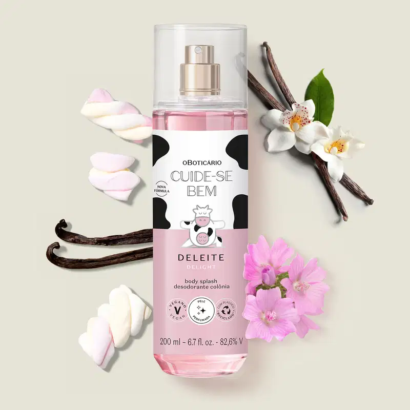 Frasco com líquido rosa, pulverizador prateado e rótulo branco e rosa com ilustração de vaca contendo 200ml de body splash Cuide-se Bem Deleite  rodeada por flores brancas, bastões de baunilha e marshmallows coloridos sobre superfície clara.