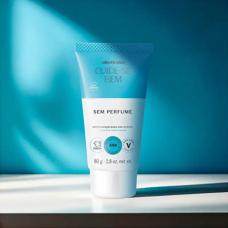 Bisnaga branca e azul com letras pretas de desodorante em creme sem perfume Cuide-se Bem em superfície branca e fundo escura em tons de azul com pouca luz natural.