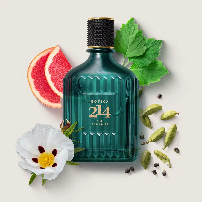 Vidro azul com textura ondulada, tampa preta e letras douradas de Eau de Parfum Fougére Especiado da marca Botica 214 Fiji Paradise com flores brancas, cardamomo verde, toranjas e folhas verdes ao redor.