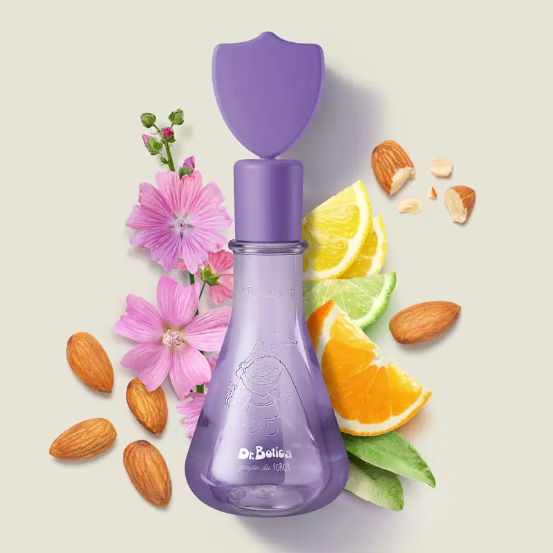 Frasco com líquido roxo, tampa com um escudo na tampa da mesma cor, contendo colônia infantil Poção da Força da marca Dr. Botica rodeado por flores rosas, fatias de cítricos e nozes, sobre superfície clara.