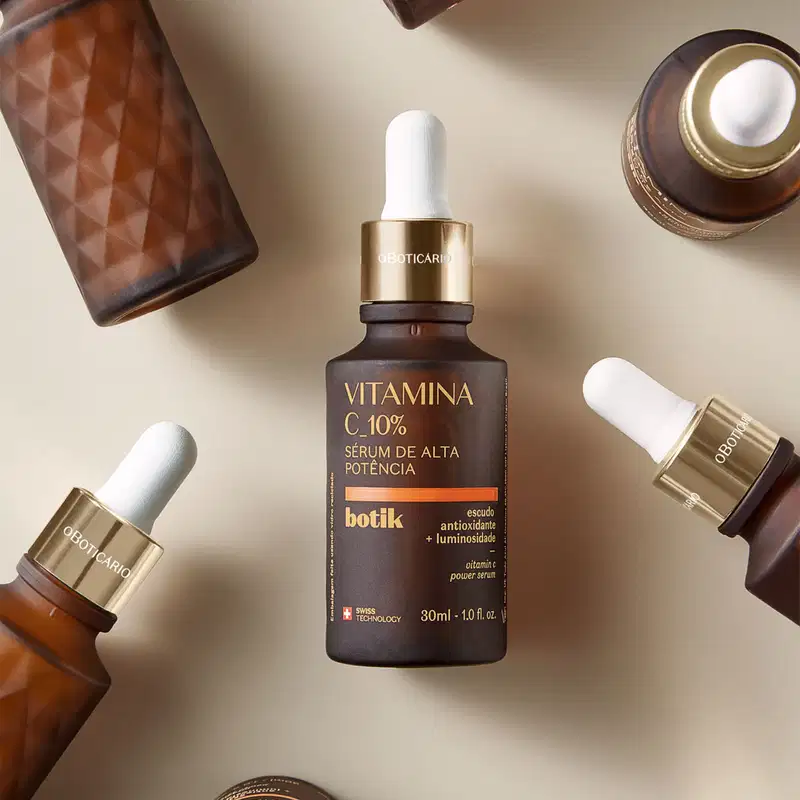 Diversos vidros marrons com detalhes dourados, conta-gotas brancos, letras amarelas e detalhes em laranja de sérum de alta potência 10% da marca Botik Vitamina C em um fundo neutro.