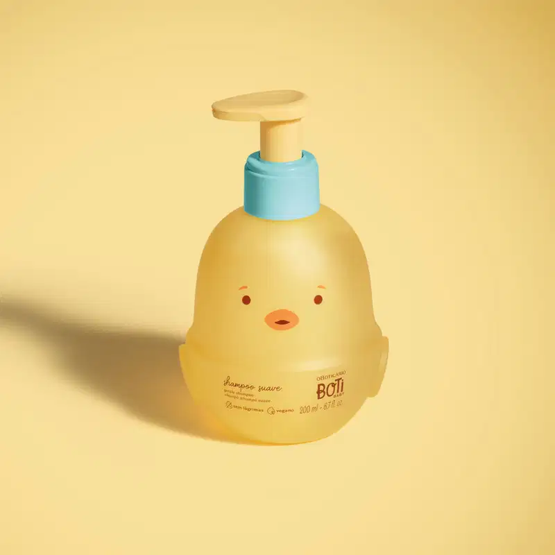 Frasco em forma de passarinho amarelo com detalhes laranjas, tampa azul e bomba dosadora amarela de shampoo suave da marca Boti Baby em fundo alaranjado.
