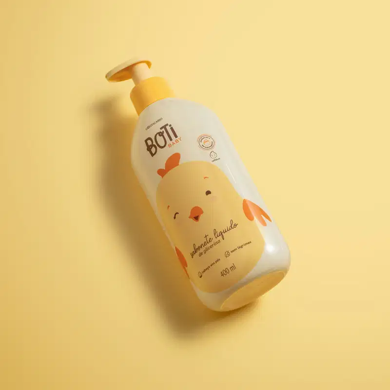 Frasco amarelo claro com ilustração de um passarinho amarelo com detalhes, tampa e bomba dosadora laranjas contendo sabonete líquido de glicerina da marca Boti Baby em fundo alaranjado.