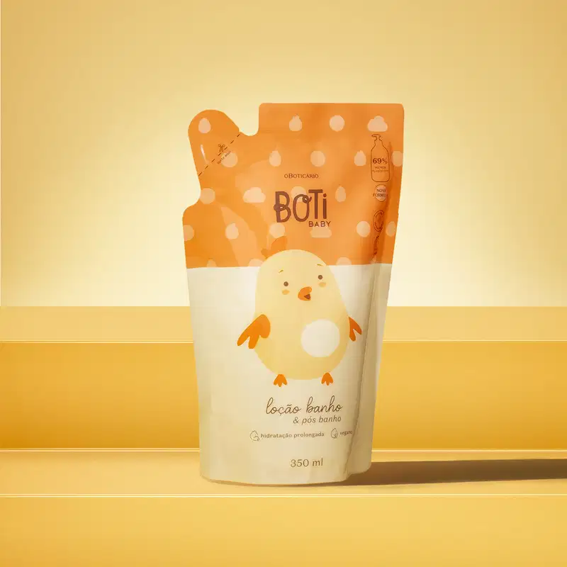 Refil de loção hidratante corporal da marca Boti Baby em forma de sachê nas cores laranja e amarelo claro com ilustração de passarinho amarelo. A imagem está em cima de uma plataforma laranja com fundo e superfície em tons alaranjados.