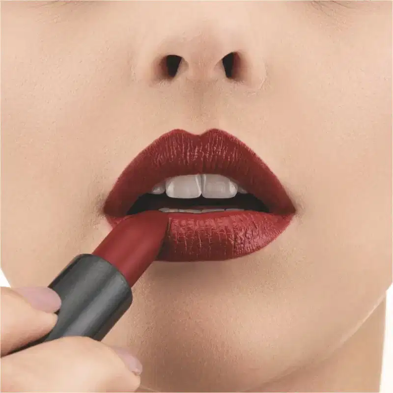 Close-up de um rosto feminino evidenciando os lábios na cor vermelho e uma mão segurando o batom cremoso na cor vermelha 340 da marca Intense.