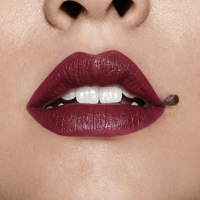 Close-up de um rosto feminino evidenciando os dentes brancos e os lábios em tom de vinho intenso que usa o batom cremoso na cor vinho 420 da marca Intense