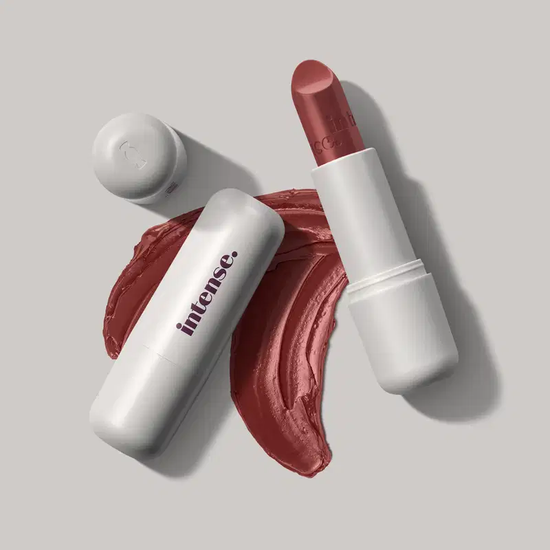 Batom cremoso na cor rosa 227 da marca Intense, em embalagem toda branca com letras pretas na tampa, com uma quantidade de produto espalhada no fundo cinza.