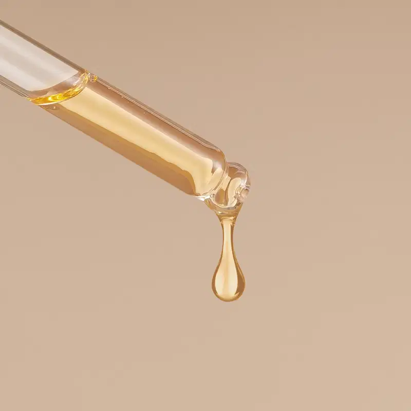 Um conta-gotas branco pinga uma gota de líquido dourado em um fundo bege.