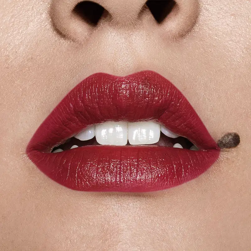 Close-up de um rosto feminino evidenciando os dentes brancos e os lábios em tom de vermelho intenso que usa o batom cremoso na cor Vermelho 310 da marca Intense
